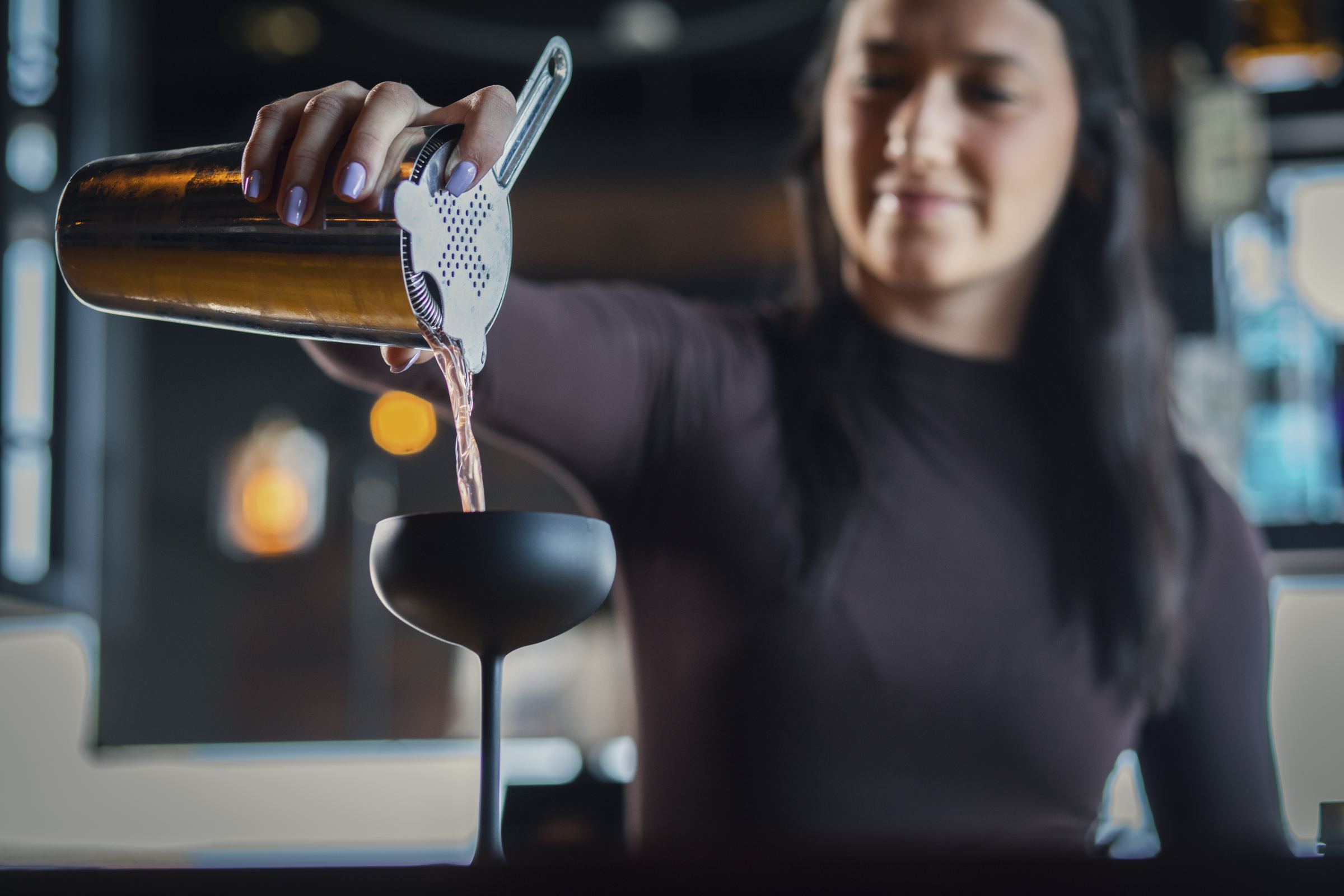 Bartender straining a cocktail into a coupe