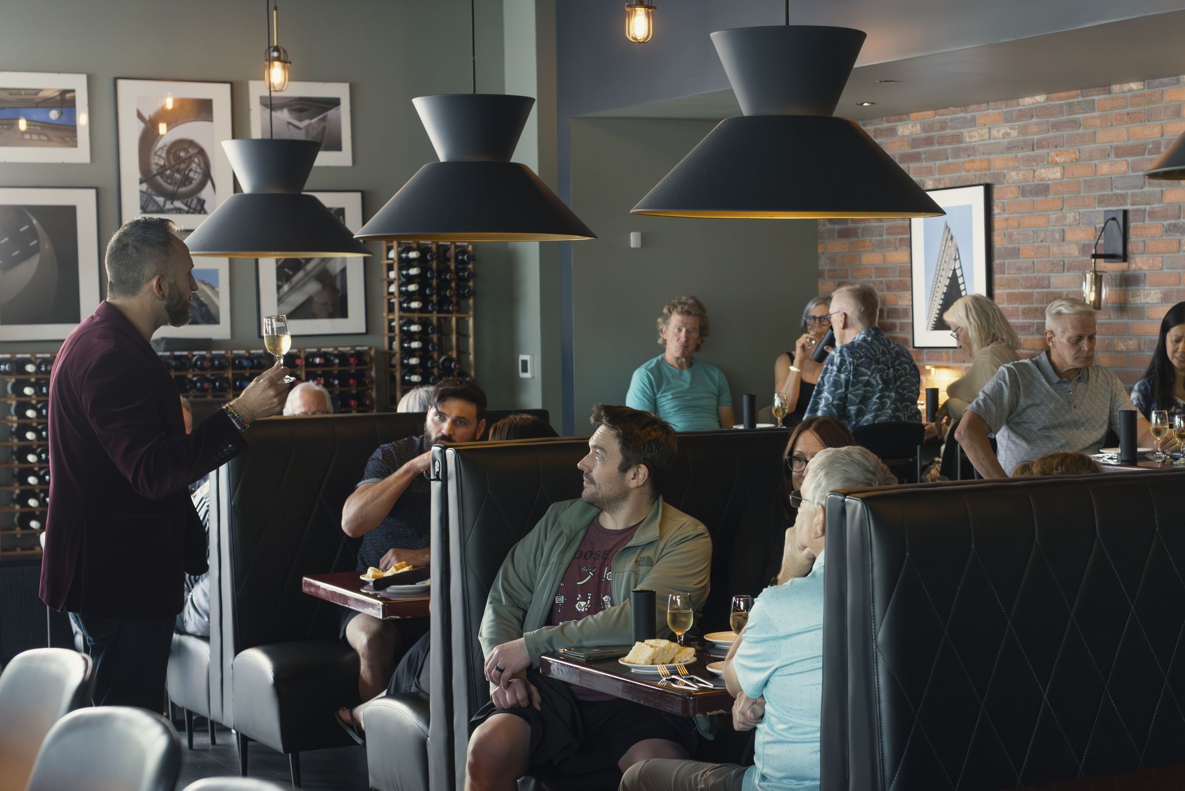 A host pouring wine for guests in a full booth